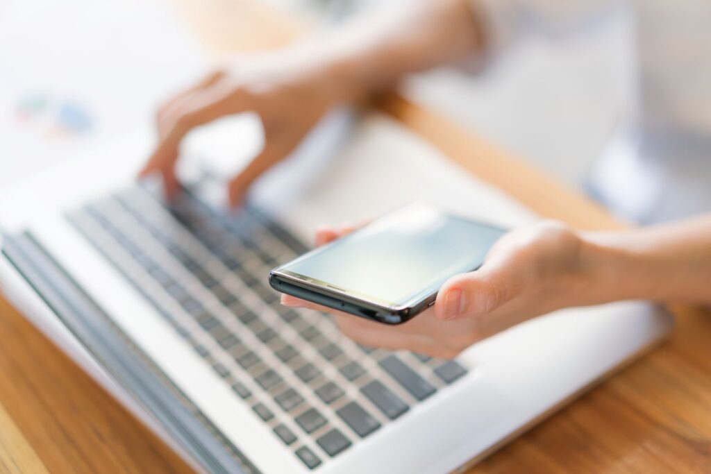 Frauenhände halten Smartphone in der Hand über der Tastatur eines Notebooks
